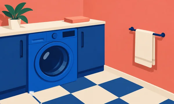 A cobalt-blue front-loading washer sits beneath a cream countertop in a coral-walled nook, with a folded coral towel, a potted plant, and a cream towel on a…