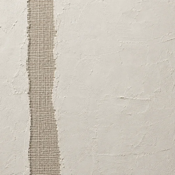 A square macro texture of warm bone-white plaster with a vertical strip of coarse flax-colored woven fabric near the left side; irregular plaster edges and…