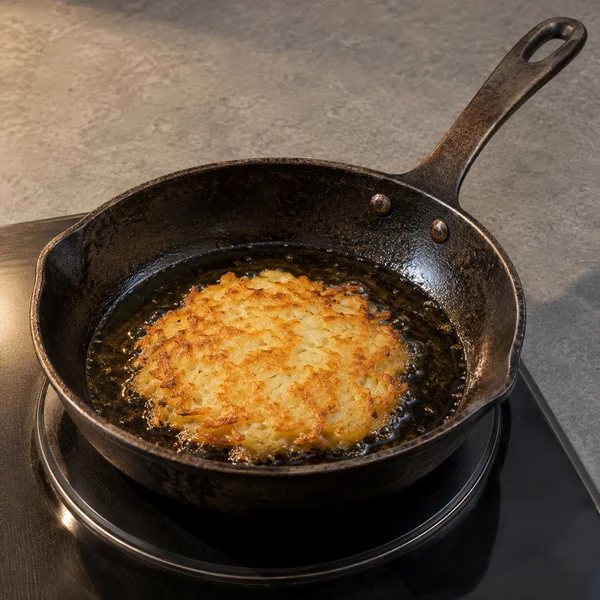 A dark, well-used iron skillet with two visible rivets sits on a black electric hob on a grey worktop.