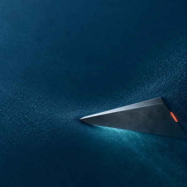 A flattened dark graphite wedge crosses the lower-right of a deep blue, finely textured field, with a cool bright bevel, a small coral-orange accent on its…