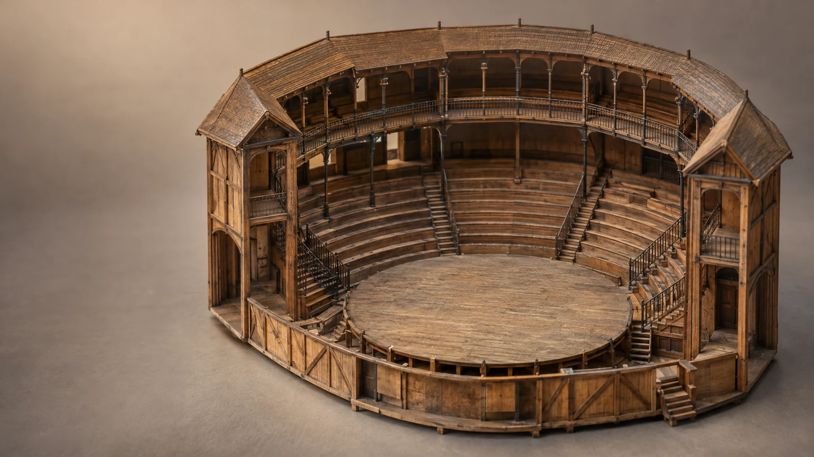 A detailed wooden scale model of an empty circular stage and surrounding tiered seating sits on a warm-gray tabletop, viewed from above against a softly…