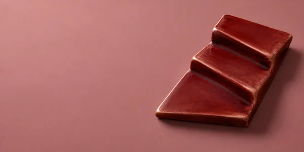 A glossy oxblood ceramic relief with three broad stepped planes sits on a dusty-rose field, casting a short dark shadow to the lower right.