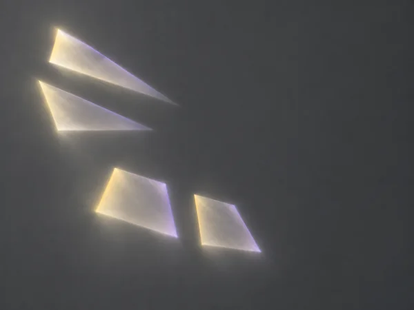 Four softly glowing geometric patches sit on a cool graphite field: two elongated triangular forms in the upper left and two shorter quadrilateral forms below…