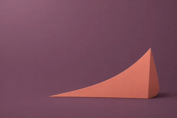 A muted coral sculptural wedge rises to a sharp apex against a dusty plum field, with a narrow darker side face and a soft contact shadow.