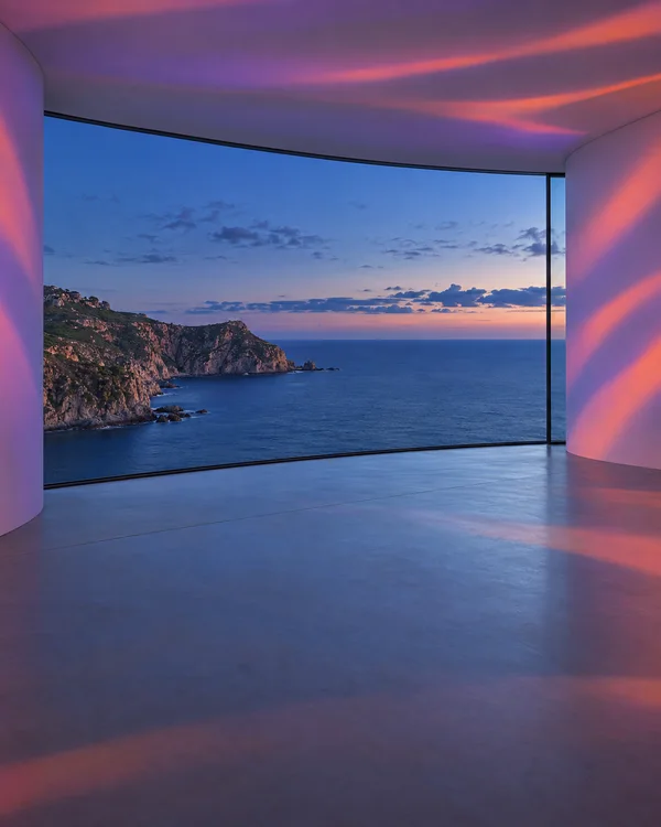 An empty curved white studio interior with a pale-grey floor and a wide glazed opening overlooking a rocky headland, calm sea and blue-hour sky.