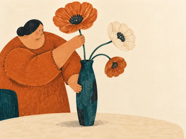 A broad person in a copper-orange smock arranges three large flowers in a tall teal vase on a cream tabletop, with open ivory space to the right.