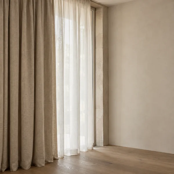 A heavy flax-colored curtain overlaps an ivory sheer beside a tall window, with a pale stone reveal, warm plaster wall and oak floor in soft daylight.