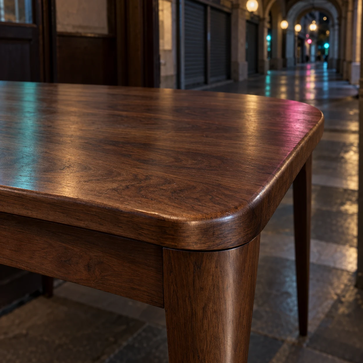 A close view of a rounded walnut dining-table corner shows its glossy wood grain, apron joint and broad tapered leg, with teal and magenta reflections; an…