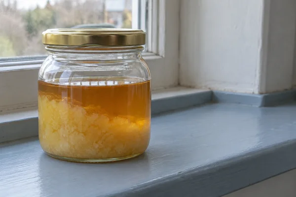 A squat clear glass jar with a gold-colored lid sits left of centre on a blue-painted windowsill.