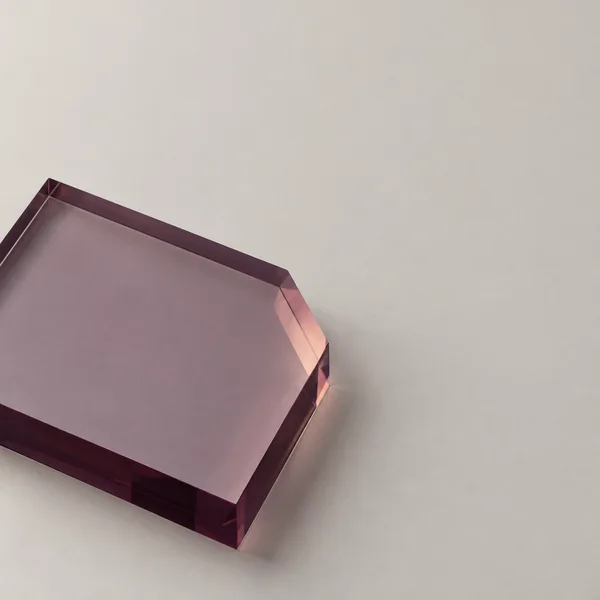 A thick translucent plum-purple rectangular slab with a pale lavender face and peach-toned bevel sits across the lower-left of a warm pale-grey field, with its…