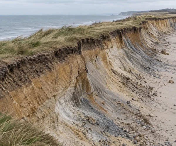 A layered coastal clay bank with a steep, crumbling face cuts diagonally across a rocky pale beach.
