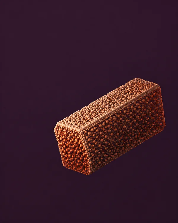 A copper-orange rectangular block made of rounded particles floats against a deep aubergine background, angled upward to the right with a peach-lit upper face…