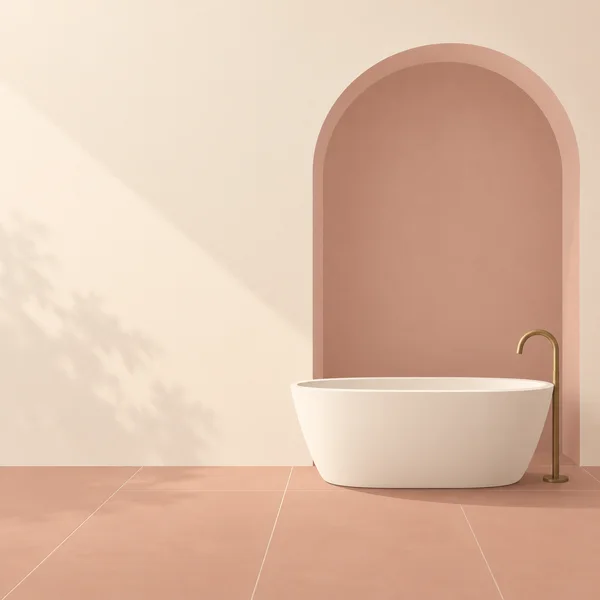 A cream freestanding bathtub sits before a tall dusty-rose arched alcove in a warm-toned bathroom, with a curved brass floor-mounted faucet and terracotta tile…