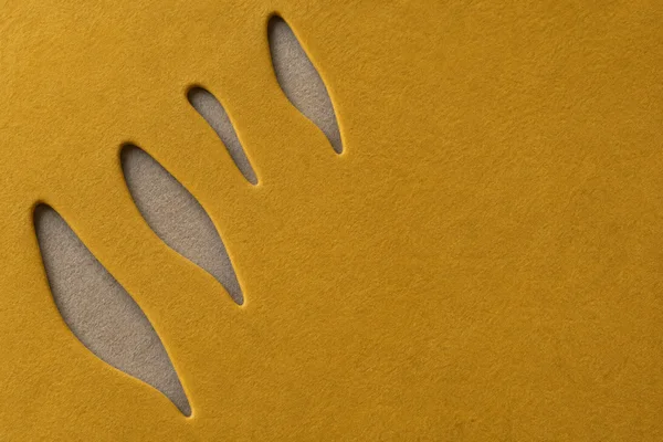 Close-up abstract textile artwork with four elongated warm-gray openings arranged diagonally across a mustard felt surface, leaving broad uninterrupted space…