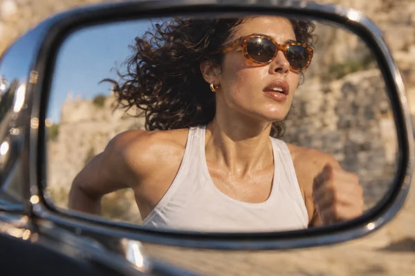 Close view of a woman running, seen in a dark chrome side mirror.