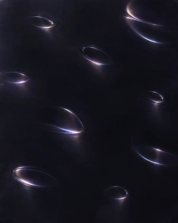 A near-black, subtly violet surface is dotted with scattered oval and crescent-shaped reflections in cool blue and soft warm light, with broad areas of…