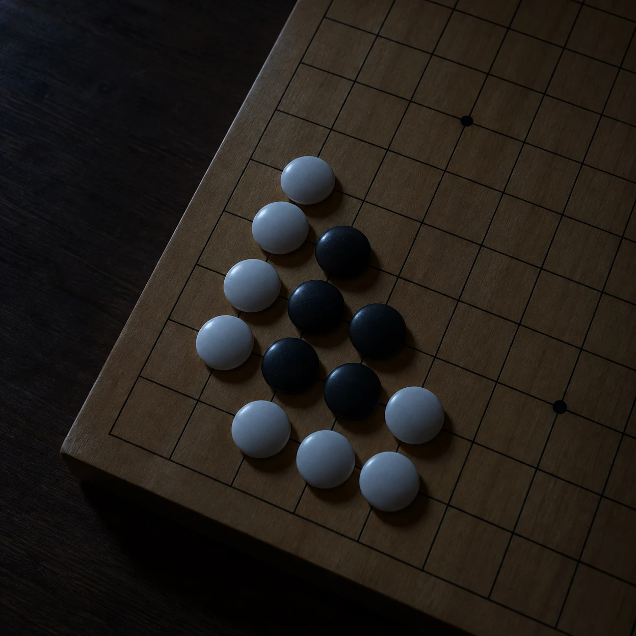 A close overhead view of white and black Go stones on a wooden grid board, with the stones lit coolly against a dark tabletop at night.