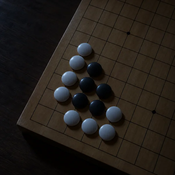 A close overhead view of white and black Go stones on a wooden grid board, with the stones lit coolly against a dark tabletop at night.