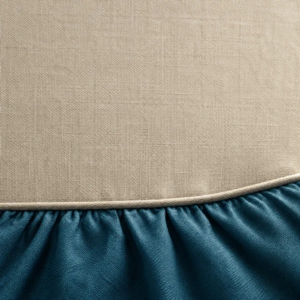 Close-up of a sand-coloured woven textile above tightly gathered petrol-blue fabric, divided by a raised seam that curves upward toward the right.