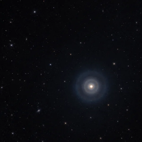 A bright ivory point glows inside soft, rounded blue and warm-toned halos in a deep, star-filled sky, positioned below and right of center.
