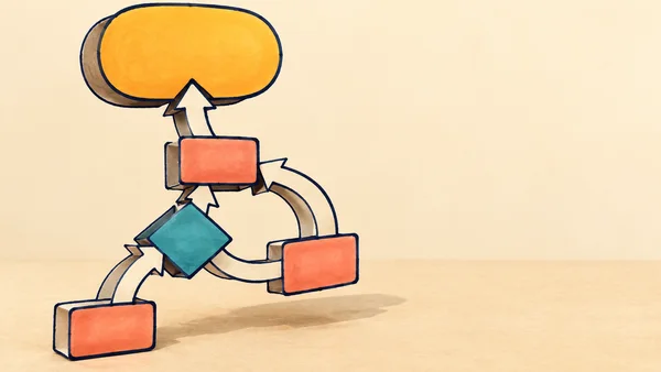 A hand-drawn paper flowchart sculpture stands above a warm cream tabletop, with coral rectangular nodes, a tilted teal diamond, a large golden endpoint, and…