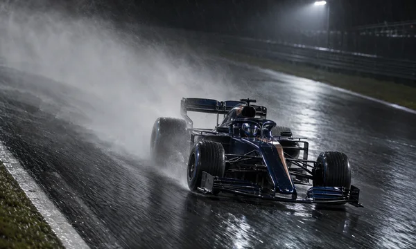 A dark blue open-wheel racing car with a copper stripe speeds across a rain-soaked circuit at night, throwing a broad spray plume behind it beneath a bright…