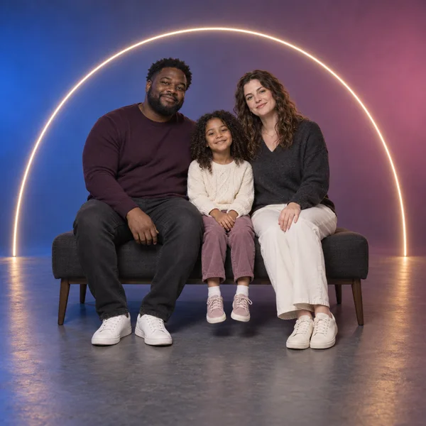 Three people sit close together on a charcoal bench against a studio backdrop washed blue on the left and rose on the right.