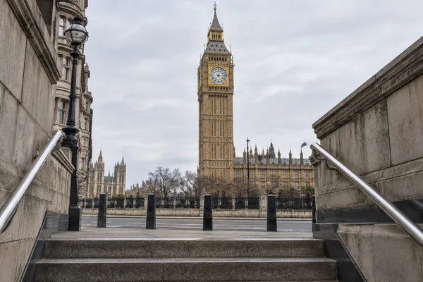 Stone steps and stainless-steel handrails frame a view of Elizabeth Tower and the Palace of Westminster beneath a pale grey sky.