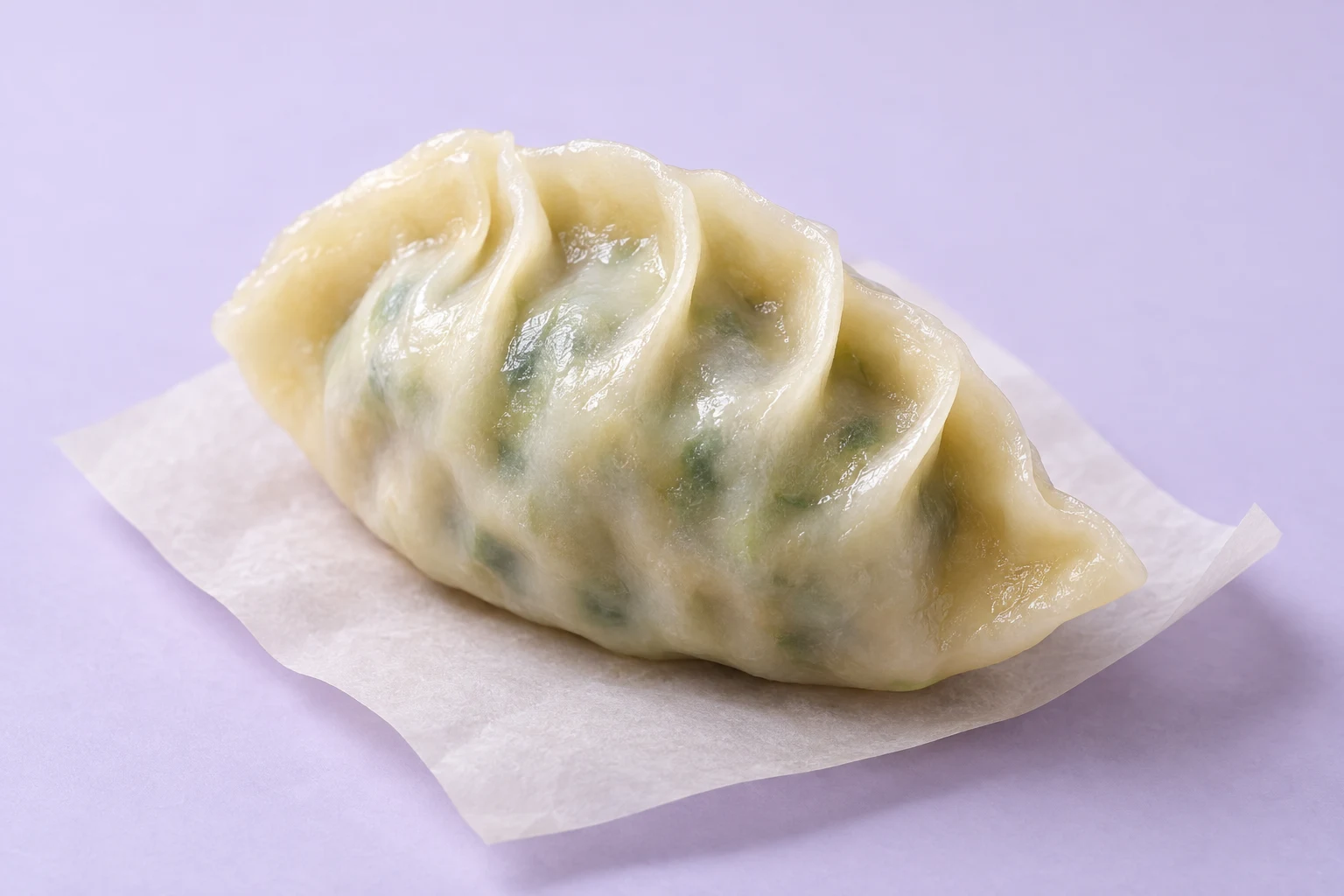 A glossy, pale crescent dumpling with visible green filling and curved pleats rests on a sheet of ivory paper against a lavender background.