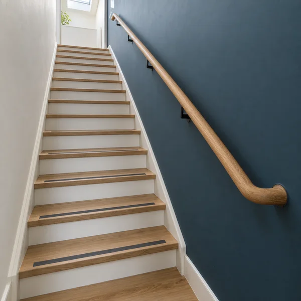 A wooden staircase with white risers and dark tread strips climbs between an off-white wall and a muted blue wall.