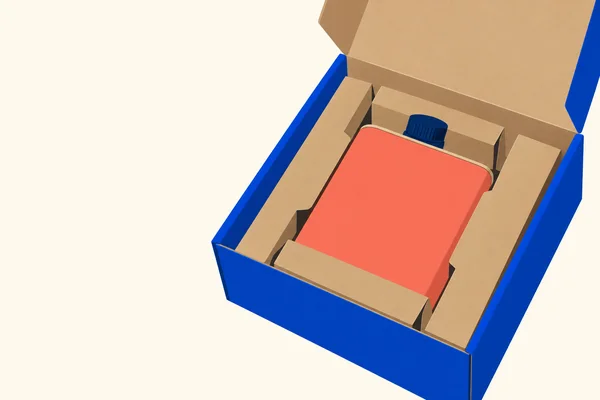 An open cobalt-blue shipping carton sits diagonally on a warm ivory surface, with a tan cardboard insert holding a coral rectangular tin with a navy screw cap.