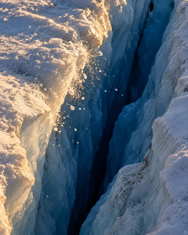 A close, elevated view into a deep cobalt-blue glacier crevasse, bordered by rough pale ice walls.