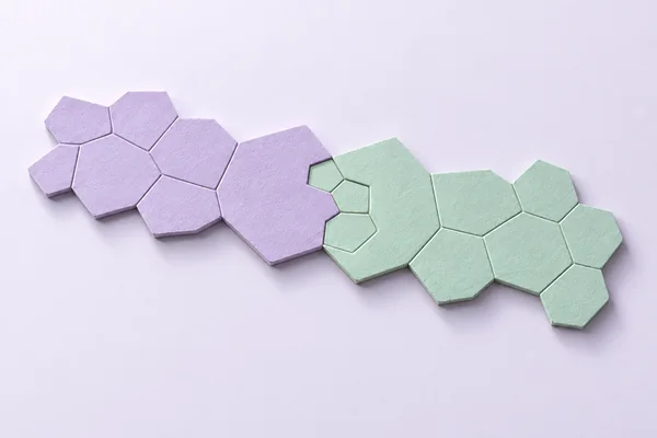 A diagonal band of lavender and mint polygonal paper tiles crosses a pale lavender surface, with three small mint tiles clustered at the central join.