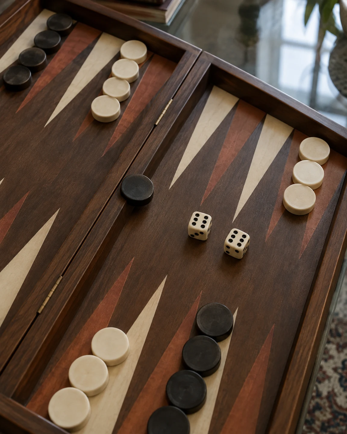 An overhead oblique view of a wooden backgammon board on a glass table, with two ivory dice showing sixes near the center, a dark checker on the bar, and ivory…