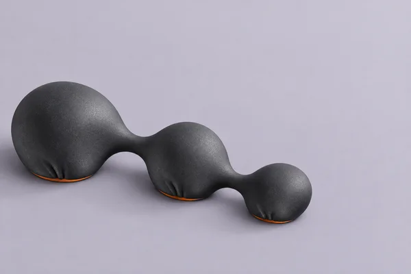A charcoal-black, three-lobed sculptural form with narrow connecting necks and thin burnt-orange edges rests on a pale lavender surface, casting soft shadows.