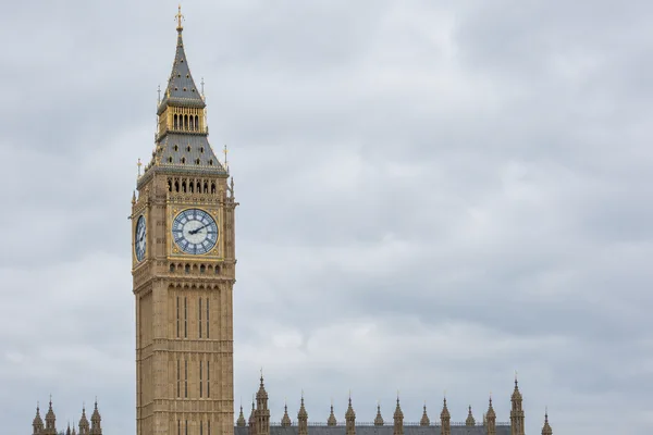 Elizabeth Tower rises left of centre beneath a pale overcast sky, with its clock faces, ornate roof and a strip of adjoining palace roof visible.
