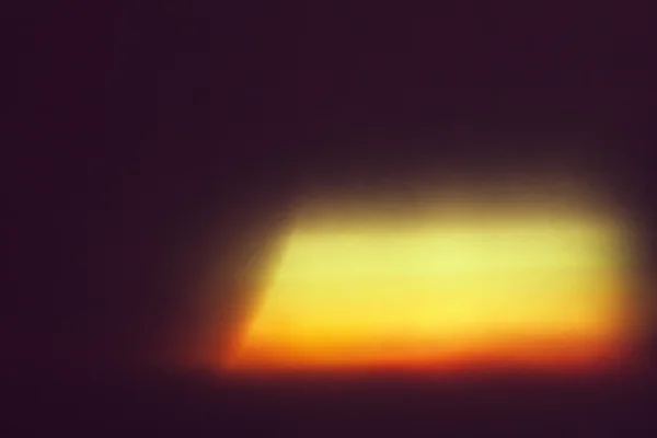 A soft, broad yellow-white light bloom with an orange glow along its lower edge floats below and right of center against a dark plum field, leaving ample open…