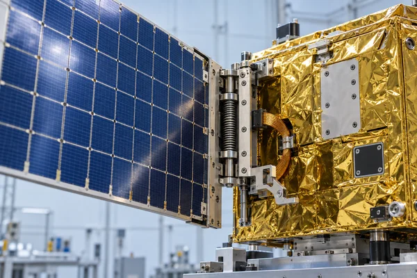 Close-up of a compact satellite with a blue gridded solar wing held partly open beside a gold-foil-wrapped chassis.