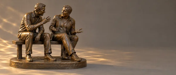 A detailed brown-bronze sculpture of two casually dressed adult figures seated together on a bench, mounted on a low oval base.