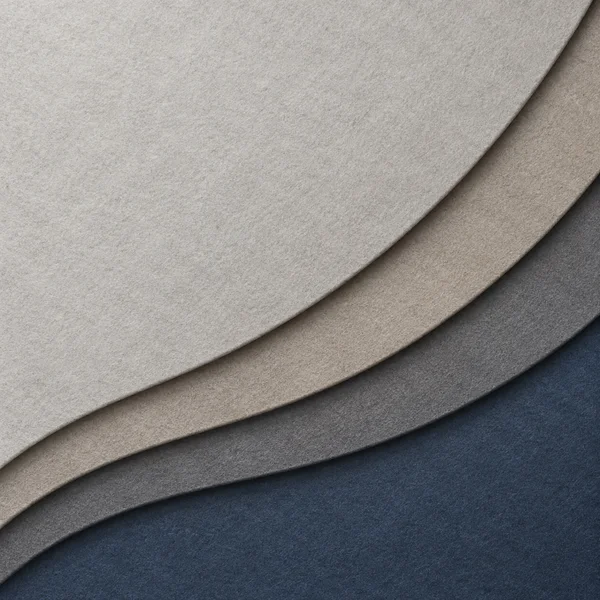 Four broad curved felt-like surfaces overlap diagonally, shifting from pale gray through warm greige and charcoal to deep blue slate, with visible fibers and…