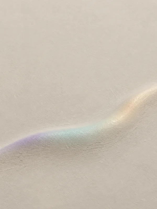 A pale putty-coloured textured surface with a shallow, asymmetrical ridge sweeping across the lower half, its crest shifting from dusty lilac through seafoam…
