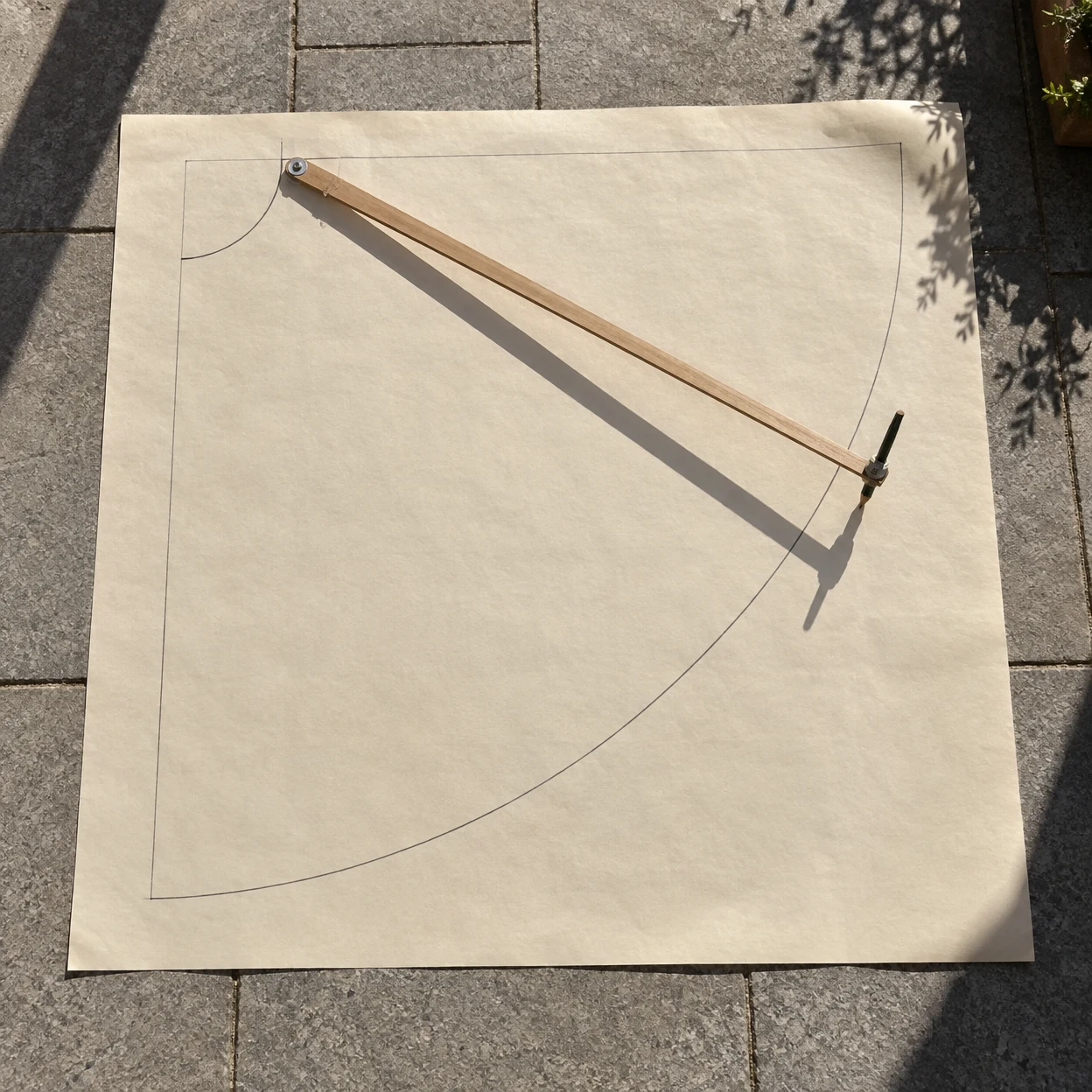 Overhead view of a large cream sheet on grey terrace paving, marked with a quarter-circle skirt pattern and a wooden beam compass resting diagonally across it…