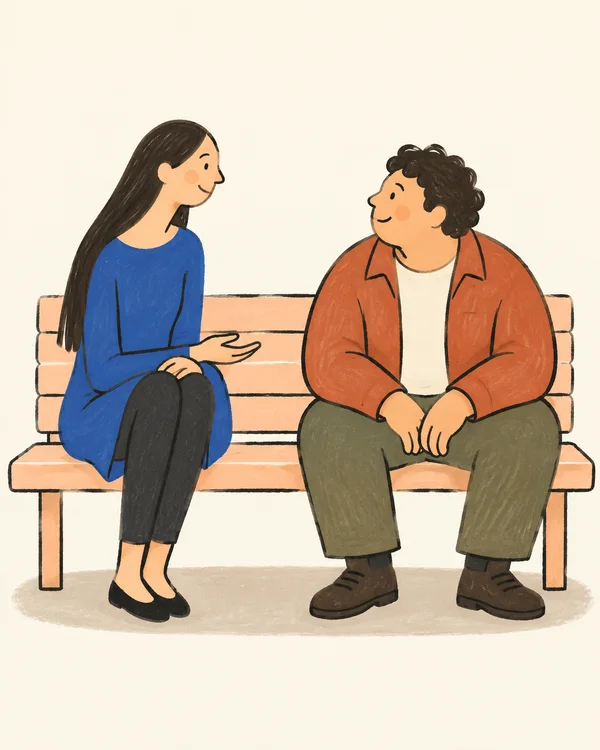 A long-haired person in a cobalt tunic and a short, curly-haired person in a terracotta jacket sit facing each other on a pale-peach park bench.