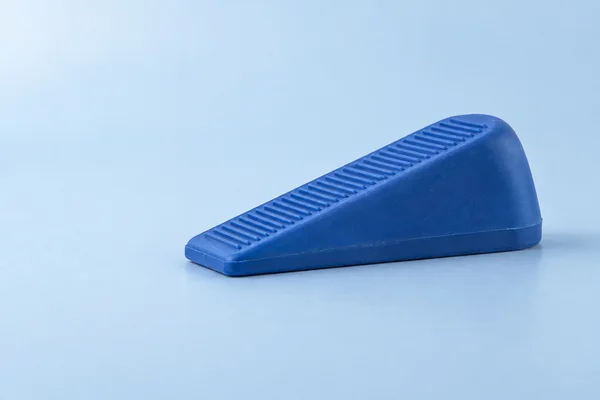A cobalt-blue rubber doorstop rests on a pale-blue tabletop, shown from a low three-quarter angle with its ribbed top and broad triangular side visible.