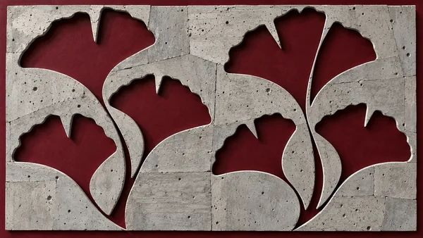 A near-frontal close-up of a pale-gray, pitted concrete screen with large fan-shaped openings over a deep oxblood backing; rectangular panel seams and dark…