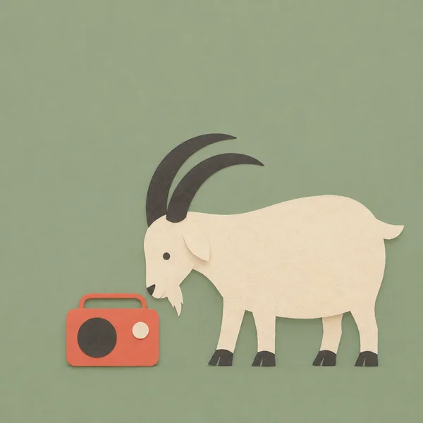 A cream cut-paper goat with large charcoal crescent horns stands in left-facing profile beside a coral radio with a dark speaker, cream knob, and raised handle…