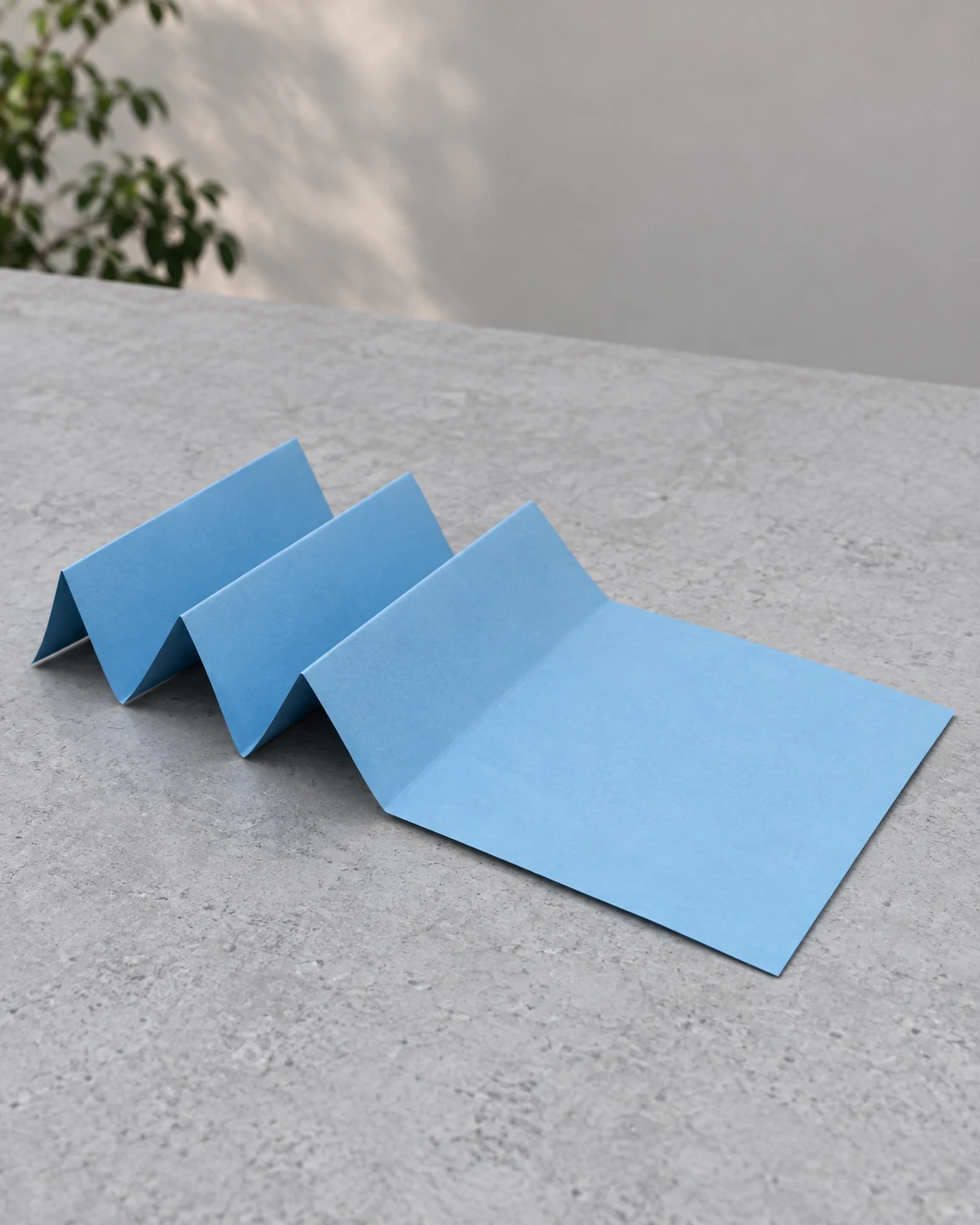 A sky-blue sheet of paper folded into three raised accordion pleats and a broad flat panel rests on a textured pale-grey tabletop.