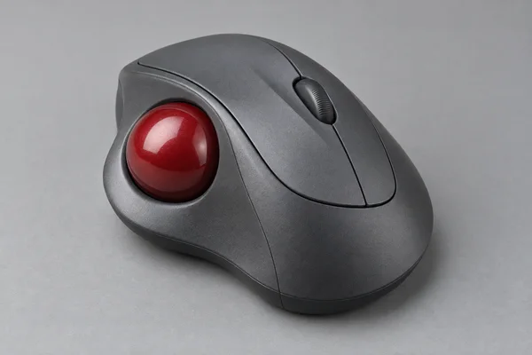 A graphite-grey wireless trackball mouse with a glossy red ball, two main buttons and a ridged scroll wheel, photographed on a cool-grey surface against a…