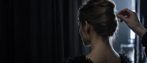 A close rear three-quarter view of a woman with a smooth updo as a hand places a hairpin into the twist.