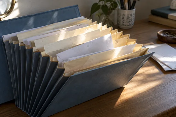 An open blue accordion file filled with cream dividers and blank envelopes sits on a wooden desk, with a loose white sheet to the right.